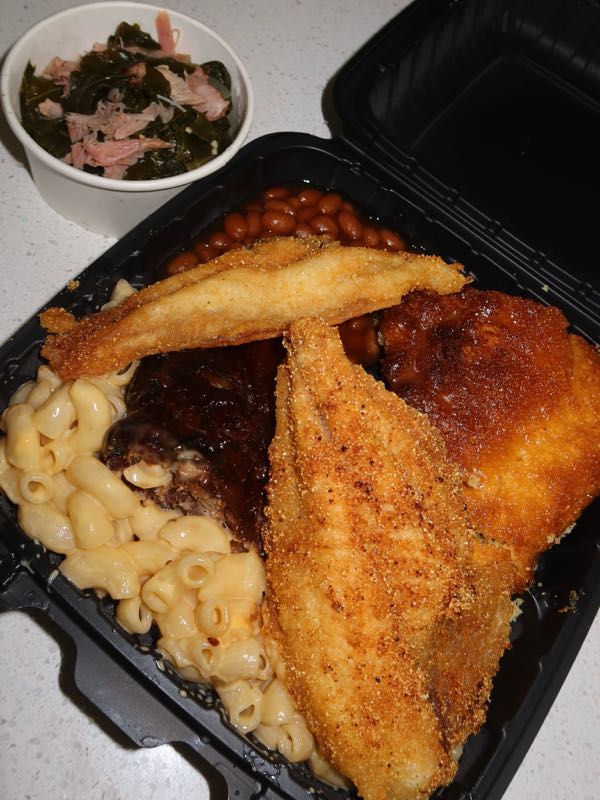 Plate of fried catfish, smoked ribs, mac and cheese, baked beans, and cornbread with a side of collard greens